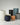 A collection of modern Eco-Fiberglass planters finished in shades of black, white, blues, brown, and gray,, in shapes including small pots to tall cylinders, on a grey and white marbled floor against a white background.