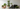 A collection of ASI fiberglass planters in various shapes and earthy tones, including terracotta, beige, white, and matte black, arranged with several green potted plants against a minimalist off-white background.
